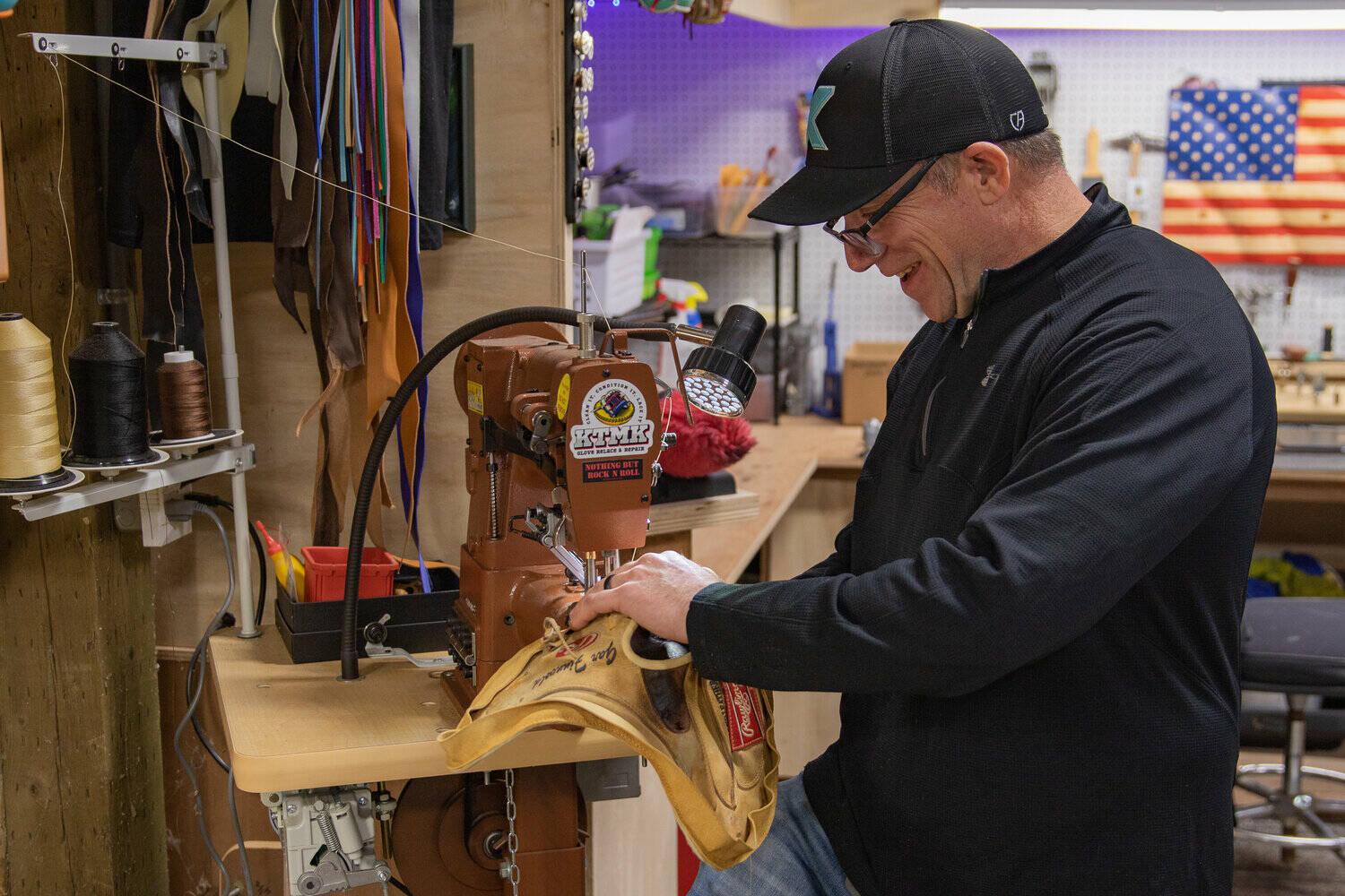KTMK Gloves founder Ken Ervin slowly guides the outer shell of a catchers mitt through a sewing machine as he puts new leather edge bindings on the mitt as part of glove restoration for a customer.