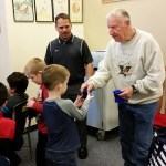Joe Cornell of the nonprofit organization &ldquo;Making a Difference for Grays Harbor Kids&rdquo; hands a pair of gloves to a student Thursday at McDermoth Elementary School in Aberdeen as Principal Brandon Winkelman looks on. (Terri Harber|The Daily World)