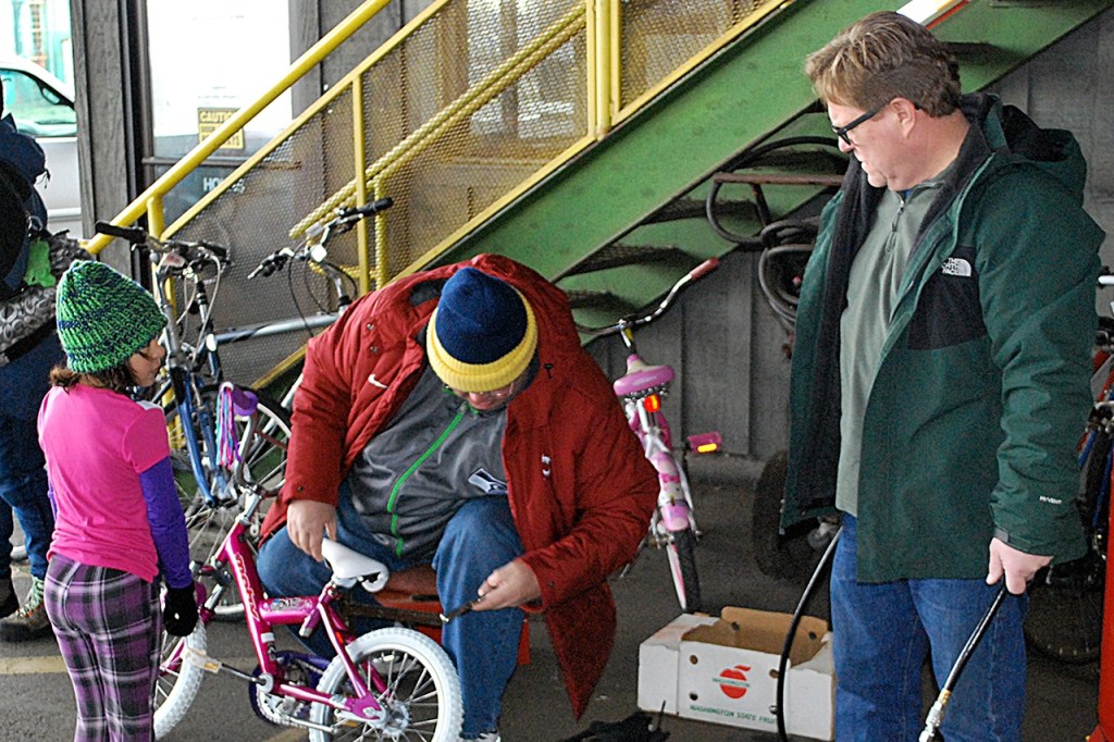 Once a child has selected a bicycle out of the 100-plus at the Bicycles from Heaven event, it is wheeled out to Lions Club volunteers who make sure the tires are properly inflated and adjust the seat for the optimum ride. Manning the air compressor at center is Bob Braden, standing to his left is Scott Berkin. DAN HAMMOCK THE DAILY WORLD
