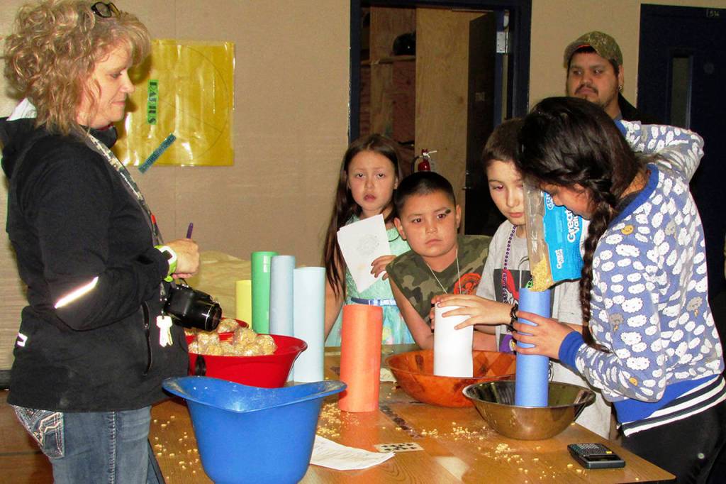 Photo by Scott d. Johnston                                Lake Quinault high school science teacher Erica Waggoner works with some of her students to estimate the volumes of various cylinders during a Pi Day activity at STEAM Family Night on March 14.