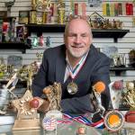Keith Baldwin, 58, president of Spike&rsquo;s Trophies in Philadelphia, displays participation trophies on the counter. Baldwin himself participated in a triathlon recently and made a participation medal (like the one hanging around his neck) for himself. (Clem Murray/Philadelphia Inquirer)