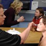 Clockwise from lower left: Karen Furth, a North River teacher, and Kristen Anderson, a friend of Heather Johnson&rsquo;s who helps out every year, apply stage makeup to fifth-grader Sierra Fuquay (Annie) and Anni Devine-Carter, a second-grader who played the orphan named July. (Photo by Kat Bryant | The Daily World)