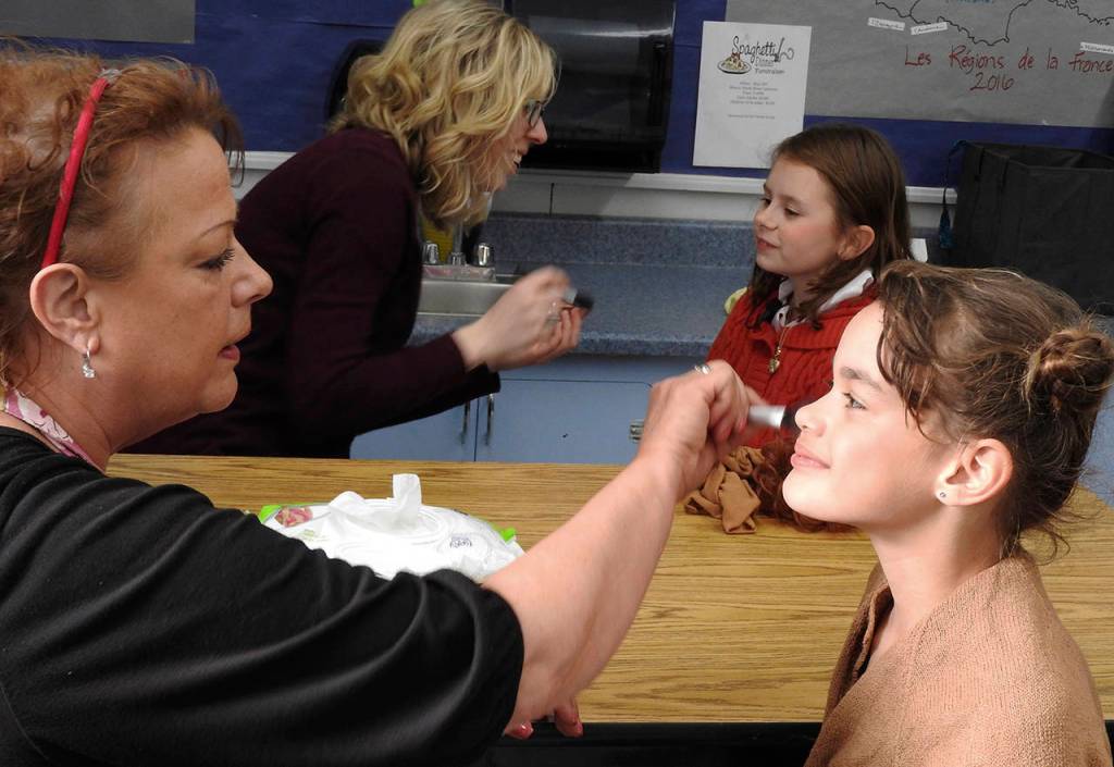 Clockwise from lower left: Karen Furth, a North River teacher, and Kristen Anderson, a friend of Heather Johnson&rsquo;s who helps out every year, apply stage makeup to fifth-grader Sierra Fuquay (Annie) and Anni Devine-Carter, a second-grader who played the orphan named July. (Photo by Kat Bryant | The Daily World)