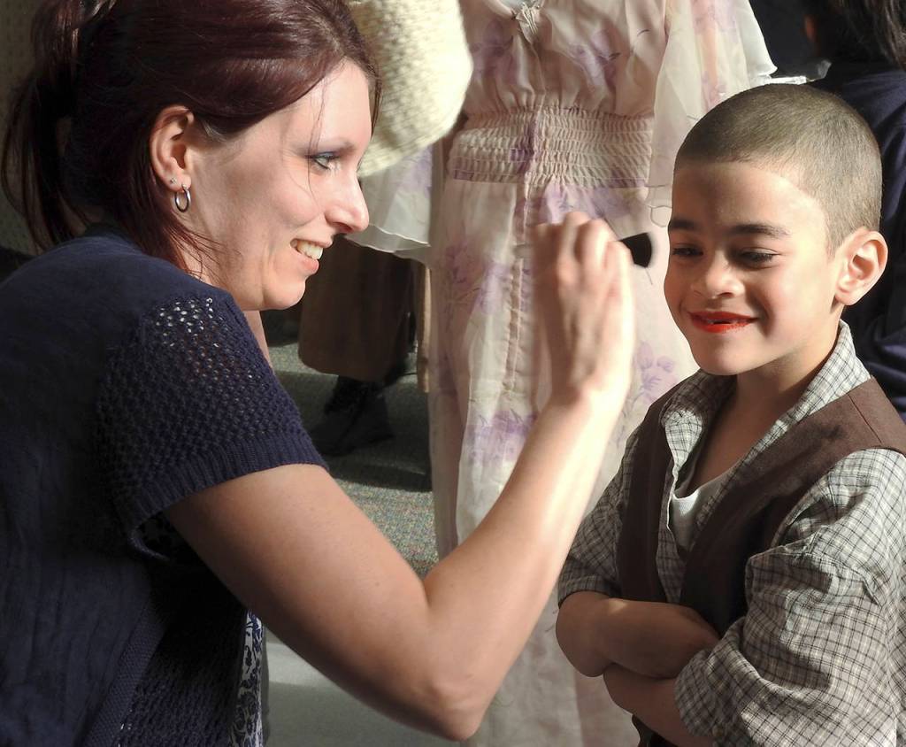 Bridget Greiner, mom of Kailey (Sandy) and Destinee (Grace Farrell), applies blush to Micah Devine-Carter, a kindergartner who played an orphan. She also helped with the spaghetti dinner beforehand. (Photo by Kat Bryant | The Daily World)