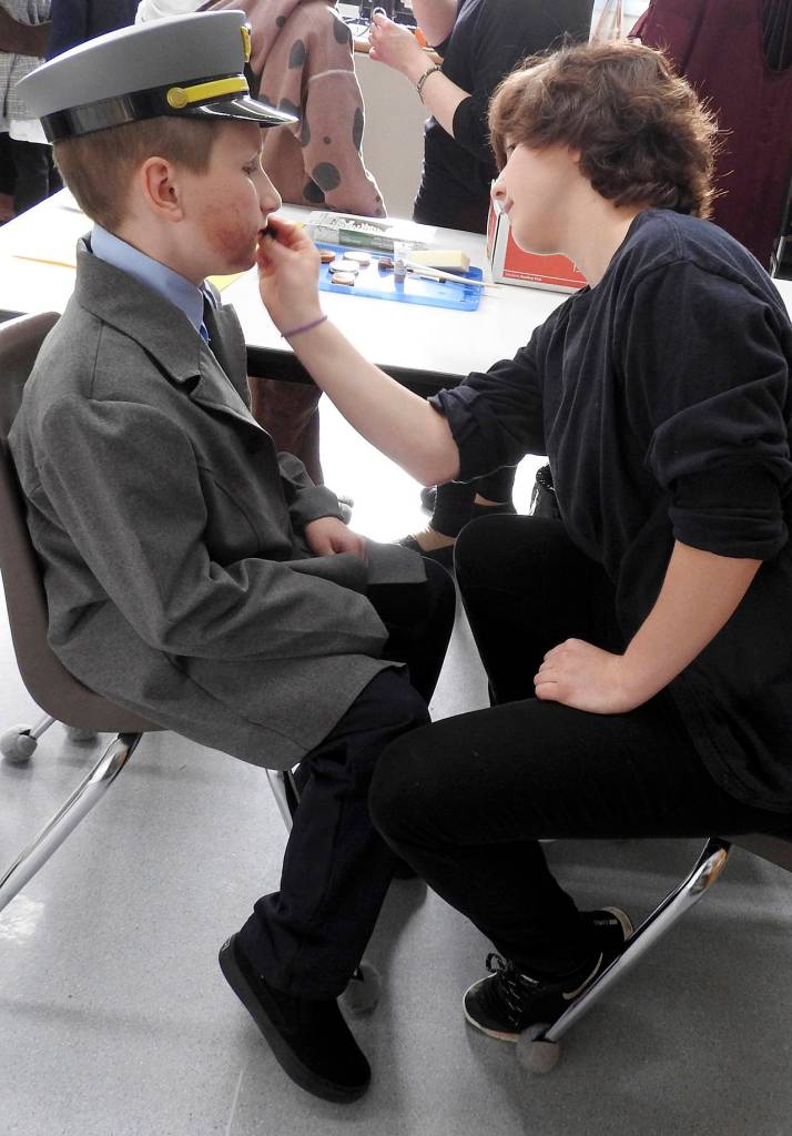 Ninth-grader Georgia Clark, who served as assistant director for &ldquo;Annie,&rdquo; paints a beard on Fischer Cain, a fifth-grader who played Lt. Ward. &ldquo;He started using a police hold on Lily and Rooster from Day One,&rdquo; laughs teacher Heather Johnson. &ldquo;We&rsquo;ve found this calling.&rdquo; (Photo by Kat Bryant | The Daily World)