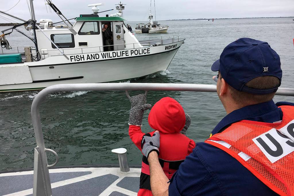 Ed Welter waves from the Fish and Wildlife Police boat to CWO Cheston Evans and his young stepson, Aiden. (Photo by Kat Bryant | The Daily World)