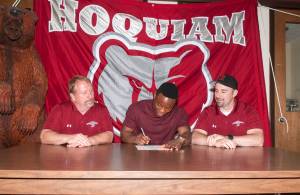 (Brendan Carl | The Daily World) Hoquiam&rsquo;s Artimus Johnson signs a letter of intent to play football at Linfield College as Grizzly coaches Rick Moore, left, and Jeremy McMillan watch on.