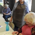 Nancy Williams watches Pam Otteson cut a design into a clay plate; behind them, Ardith Forsgren draws a design to paint onto a bowl. All are members of the North Beach Artists Guild in Ocean Shores. (Kat Bryant | The Daily World)