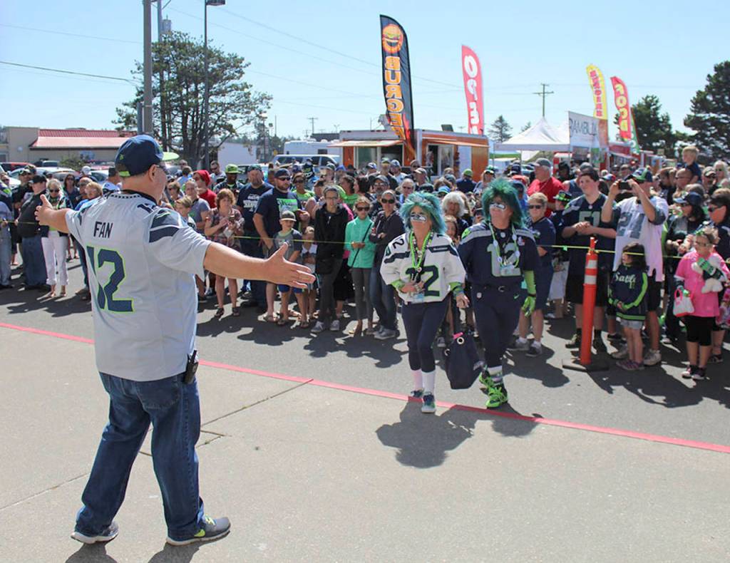 TOP: Seahawks gear for every taste will be on display at the Seahawks Fan Fest this weekend.. BOTTOM: Event organizer Terry Johnson of the Mighty 12&rsquo;s Alliance Seahawks fan organization greets Mr. and Mrs. Seahawk (Jeff and DeDe Schumaier of Auburn) before the raising of the 12th Man flag at last year&rsquo;s Fan Fest.