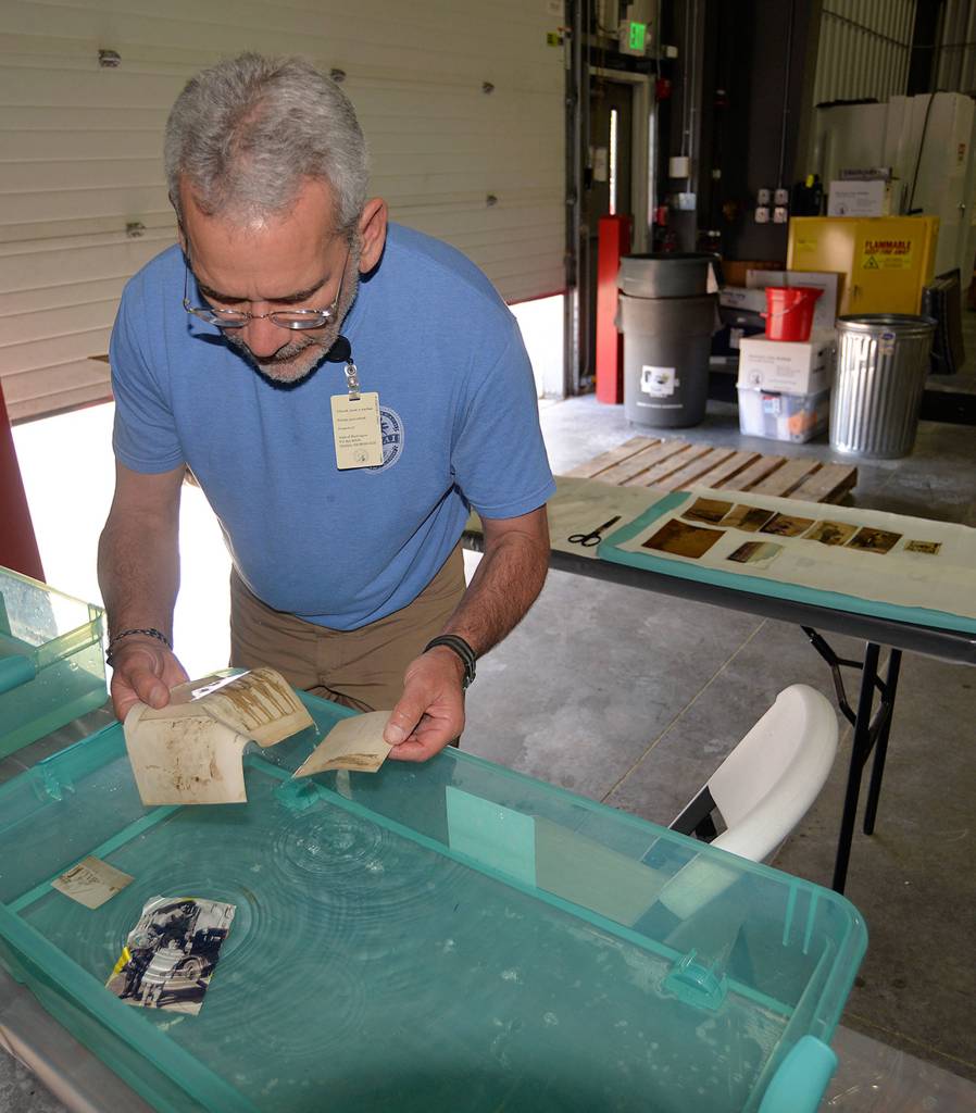 Gary Bortel, a volunteer from the Washington State Library, separates and cleans photos from the Aberdeen Museum of History in a tub of water.