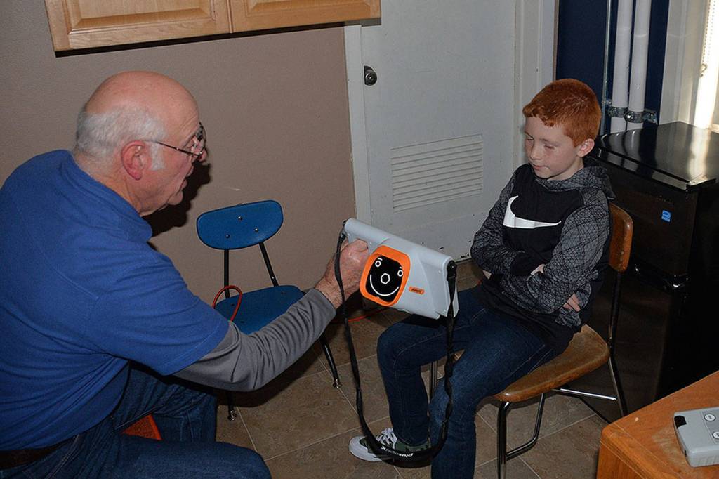 Louis Krauss | The Daily World                                Lions Club member Erv Granahan, left shows a Stevens Elementary student the vision screener report after scanning his eyes with it.