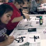 (Courtesy photo) From left, Brielda Manu, Aliyah Tageant and Savannah Hendricks practice Japanese calligraphy with their classmates at AHS.