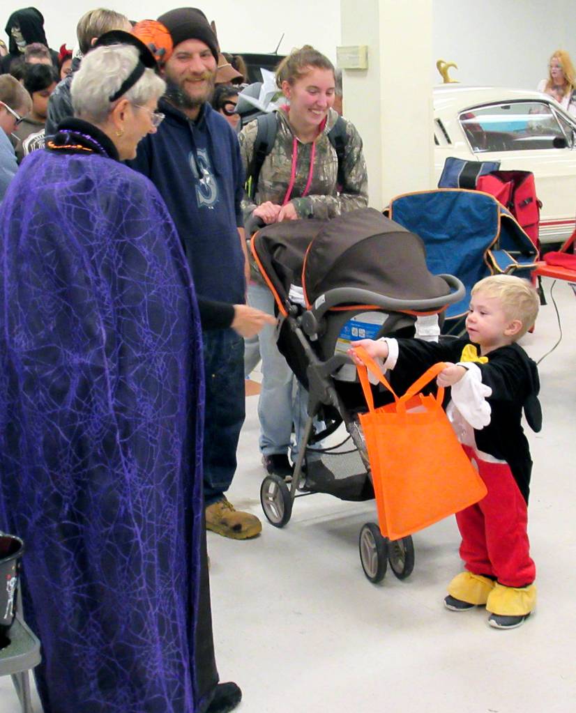 Ila Myers hands candy to a little Mickey Mouse. She and her husband, Mike, of Cosmopolis, adorned their Ford Mustang with webbing and spiders.