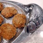 (Mitchell Chapman) Salmon cakes served on a textured Bruce Fox Designs oval tray with two salmon sculpture handles.