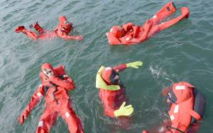 ZACH CRAWFORD | US COAST GUARD                                Mike Rudolph, in yellow gloves, a fishing vessel safety examiner from the Coast Guards Marine Safety Unit Portland, teaches students how to move around more efficiently in their survival suits during an 18-hour drill conductors course in Newport, Ore.