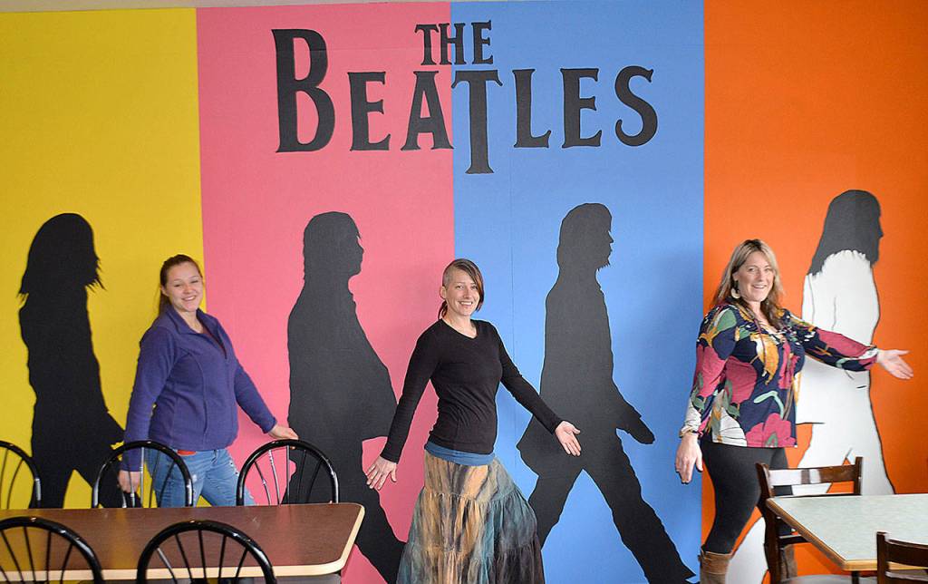 DAN HAMMOCK | GRAYS HARBOR NEWS GROUP                                Westport artist Nina Yates, center, blends into her mural of The Beatles with fellow artist Kemi Strode, left, and RocknBrews owner Cindy Perry. Yates blended the iconic Abbey Road album cover with background colors based on pop artist Andy Warhols cover for the 1980 book, The Beatles, to create the mural.