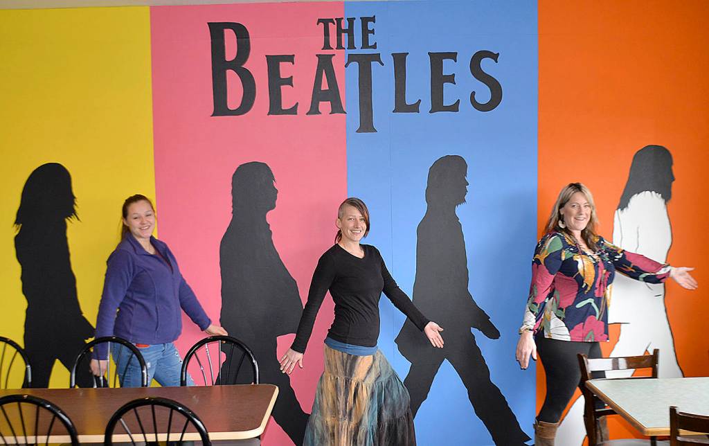 DAN HAMMOCK | GRAYS HARBOR NEWS GROUP                                Westport artist Nina Yates, center, blends into her mural of The Beatles with fellow artist Kemi Strode, left, and RocknBrews owner Cindy Perry. Yates blended the iconic Abbey Road album cover with background colors based on pop artist Andy Warhols cover for the 1980 book, The Beatles, to create the mural.