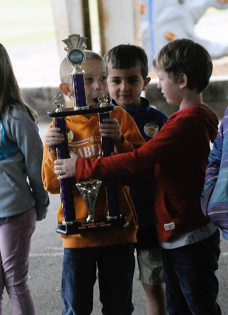 Emerson Elementary School students Ashton Balesteri, orange sweater, and Dayton Keys, red sweater, admire a trophy won by race car driver Zack Simpson on Vehicle Day on June 13. (Hasani Grayson | Grays Harbor News Group)