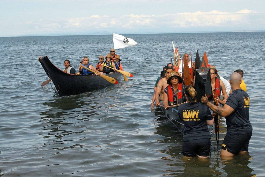 A canoe from Mowachaht First Nation, left, pulls up next to a Makah tribal canoe during Tuesdays 2019 Canoe Journey landing at Jamestown Beach, territory of the Jamestown SKlallam Tribe. (Keith Thorpe/Peninsula Daily News)