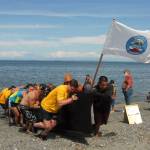 Crew members, with assistance from U.S. Navy personnel from Naval Base Kitsap, push a Quinault tribal canoe onto Jamestown Beach on Tuesday. (Keith Thorpe/Peninsula Daily News)