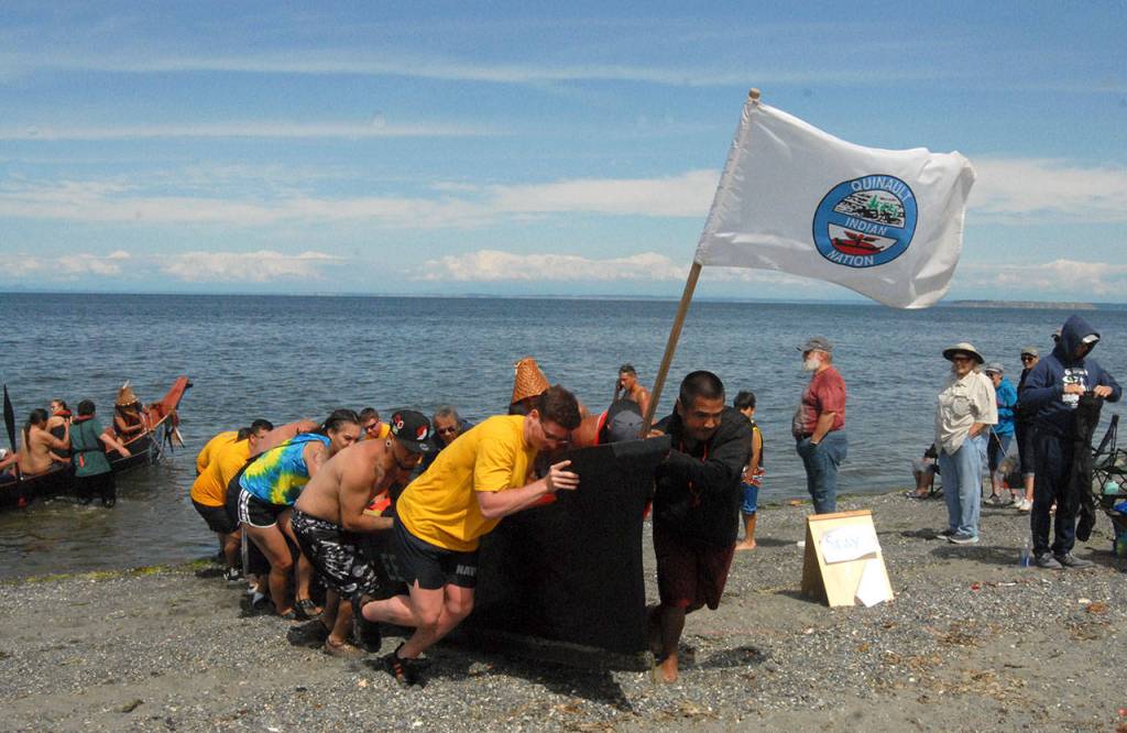Crew members, with assistance from U.S. Navy personnel from Naval Base Kitsap, push a Quinault tribal canoe onto Jamestown Beach on Tuesday. (Keith Thorpe/Peninsula Daily News)