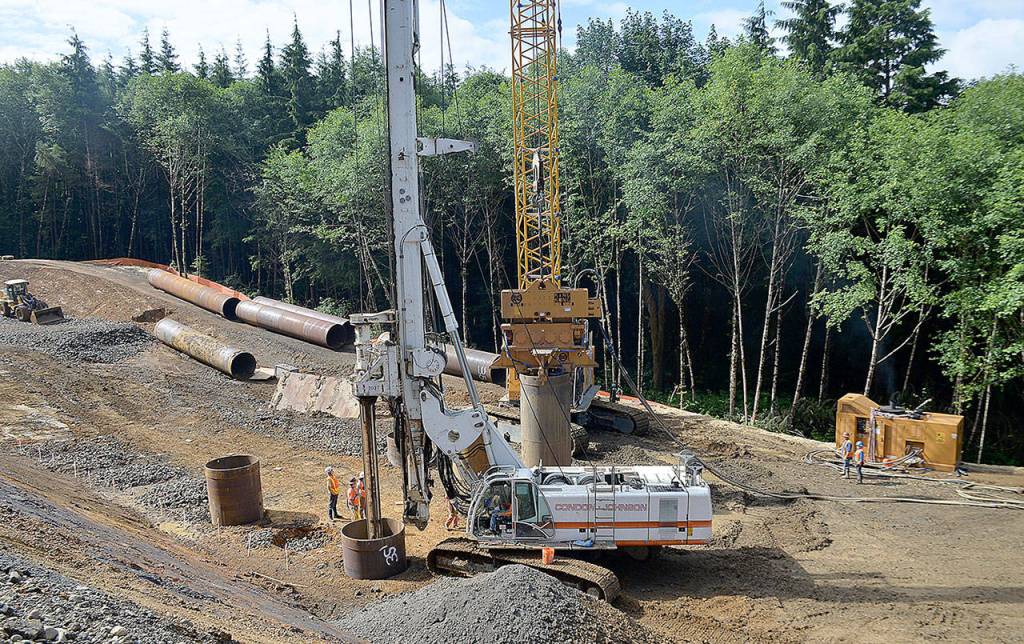 DAN HAMMOCK | GRAYS HARBOR NEWS GROUP                                The busy Cosi Hill stabilization site is making headway. At left, dump trucks enter and dump off loads of cobble and take away loads of soil removed by drilling. The white crane in the center drills the holes  575 when its all said and done  and the yellow crane behind it uses a vibrating weight to drive in the shafts that will hold the cobble temporarily.