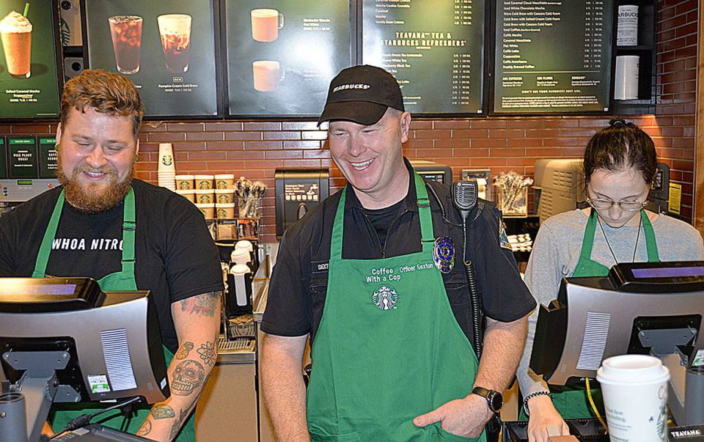Aberdeen Police Officer Gary Sexton, center, is flanked by Starbucks employees Zach Grebenc and Holly Bergeson as he mans the register at the Wishkah Street Starbucks during the Coffee with a Cop event.
