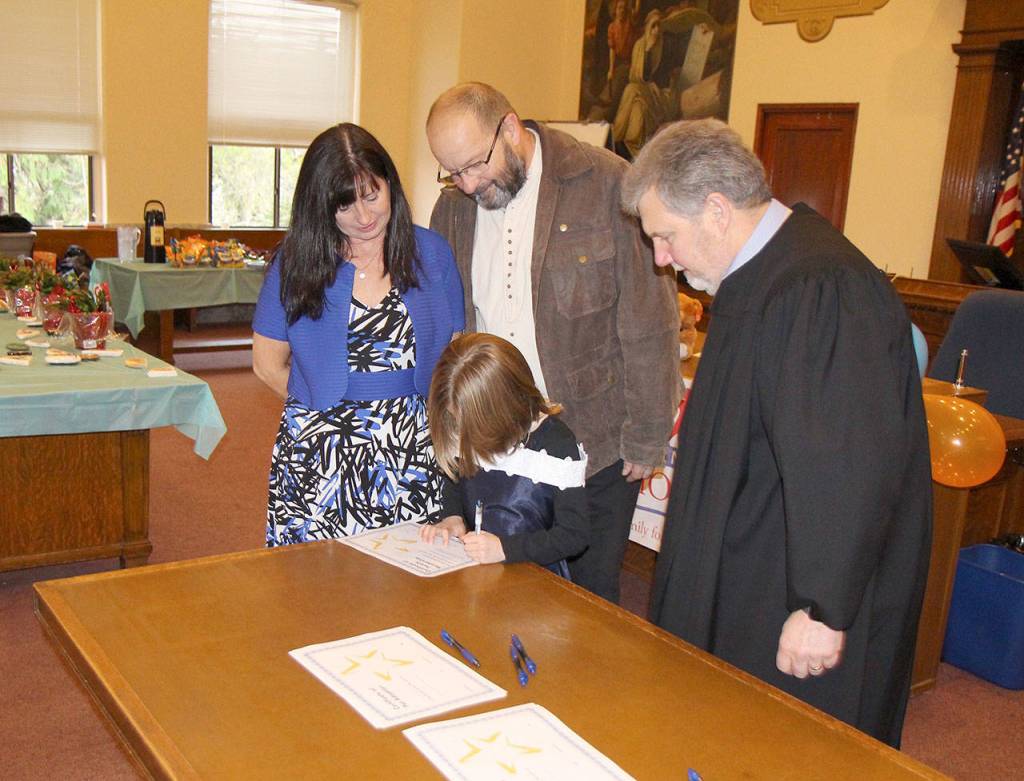 Gianna signs her adoption certificate while her new parents and Judge Stephen Brown watch Friday during the National Adoption Day ceremony in Judge Stephen Browns courtroom at Grays Harbor County Superior Court in Montesano. (Michael Lang | Grays Harbor News Group)