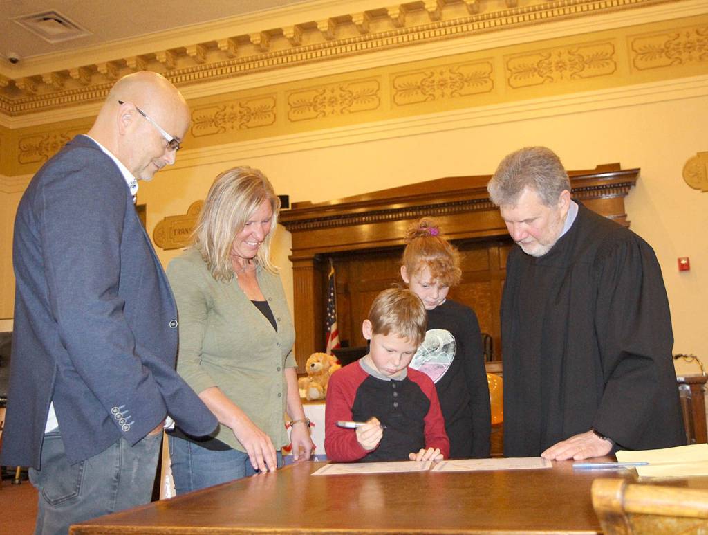 The Robles family  Sean (from left), Terri, Eric and Julianna  watches as Eric finishes signing an adoption certificate Friday during the National Adoption Day ceremony in Judge Stephen Browns courtroom at Grays Harbor County Superior Court in Montesano. (Michael Lang | Grays Harbor News Group)