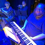 In the blue-lit wings, from left, are Connie Bevington providing the sound of the magic flute, Jessica Jurasin on piccolo to represent Papagenos pipes, and Alex Eddy on keyboard creating the sound of the magic bells.