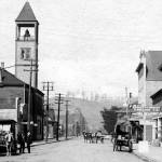 J Street looking north from 8th Street. As the second wave of influenza hit Hoquiam in early December, this block was ground zero for treating the ill at the emergency hospital set up in the Fraternal Order of Eagles hall at 709 J Street. The buildings F.O.E. entrance sign is partially obscured behind the Hackett-Corkery Logging Co. sign at right. Hoquiams City Hall at the time was on the left with the bell tower.