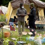 Erika Schultz | Seattle Times                                 Marcus Henderson, center left, talks with Adam Powers at the gardens at the Capitol Hill Autonomous Zone (CHAZ) in Seattle on Saturday. Henderson is organizing the large-scale gardening operations at Cal Anderson Park.