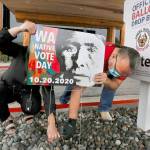 Lummi tribal members Teresa Taylor and Freddie Lane secure a Washington Native Vote Day sign outside the tribes Administration Building on October 7, 2020, north of Bellingham, Washington. The image on the sign is one by Edward Curtis titled Lummi Woman from 1899, modified to encourage Lummi tribal members to vote. (Alan Berner/Seattle Times/TNS)