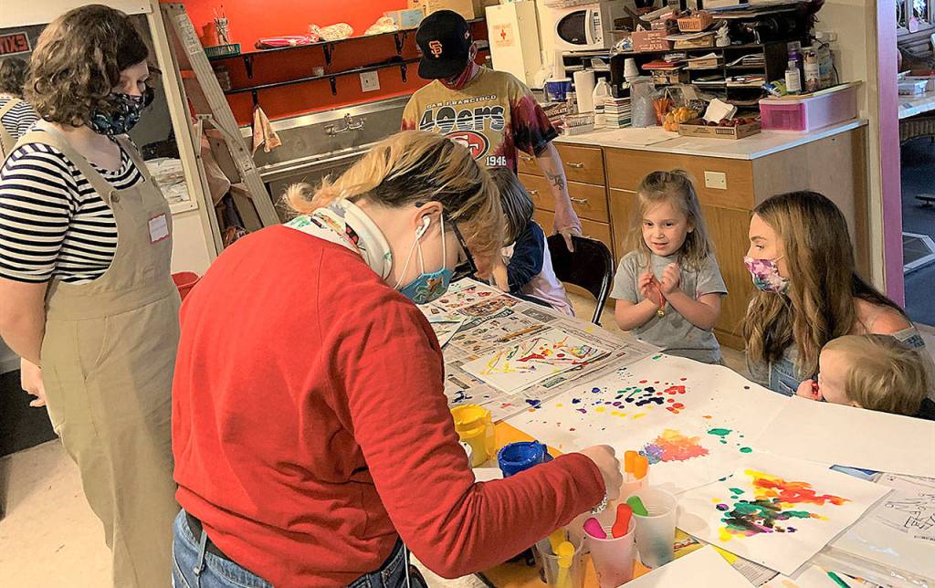 Aberdeen High School senior Delaney Olson (foreground) helps Mae Gambee, 4, choose a new color to add to her artwork on Saturday at the Cosi Art Center. Mae is with her mom, Sarah Gambee, and baby brother Grant. (Kat Bryant | The Daily World)