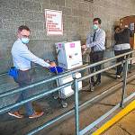 UWMC Montlake campus Pharmacy Administration Resident Derek Pohlmeyer, left, and UWMC Pharmacy Director Michael Alwan transport a box containing the Pfizer coronavirus vaccines toward a waiting vehicle headed to the UW Medicines other hospital campuses on Monday morning. These are among the first to be distributed in Washington state. (Pool Photo)