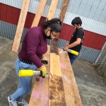 courtesy photo 
Ocosta Junior-Senior High School students Lidia Morales, a junior, and Cyrus Cardreon, a senior, burn wood planks, in order to preserve them, during their plank house trailer project.