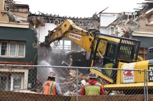 Matthew N. Wells | The Daily World
Ascendent Demolition workers Dylan King, left, works a water hose for dust control while Jason Mellick, right, operates a shovel machine with a grapple in order to safely destroy the Grays Harbor Transportation Authority building at 300 E. Wishkah Street. The 118 1/2 address is the buildings South H Street address. Joe Munoz, center, supervised the operation, which started at about 8:30 a.m. Tuesday. Jamie Kerlee, a demolition expert and one of the onlookers standing on the sidewalk across from the site, was impressed by how careful the crew worked. Theyre doing a good job, said Kerlee, who has 20 years of experience in demolition work. Hes doing the right thing. Once he gets in there, hell be able to get to the soft debris and concrete. Jasons a very good operator. Hes very skilled.