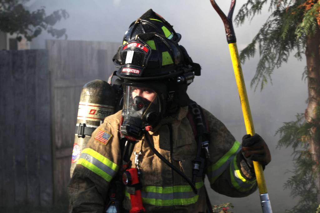 A firefighter responding to an Elma structure fire takes a moment from ripping siding off a mobile home on Nov. 15. (Michael S. Lockett / The Daily World)
