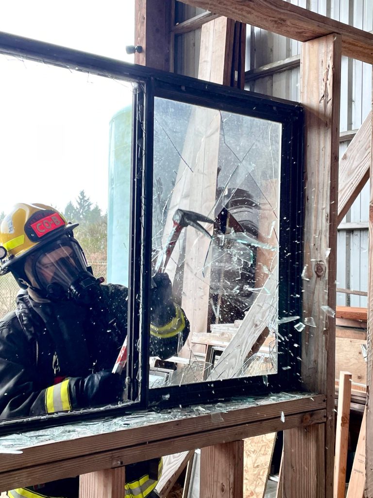 A volunteer firefighter practices breaching through a window before clearing the edges of the frame of fragments during a firefighter academy in Westport on Feb. 18. (Michael S. Lockett / The Daily World)