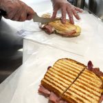 Shelly Dixon, after pulling off a freshly-grilled breakfast sandwich from the press, cuts into The Cuban sandwich, which comes with six ounces of pulled pork.