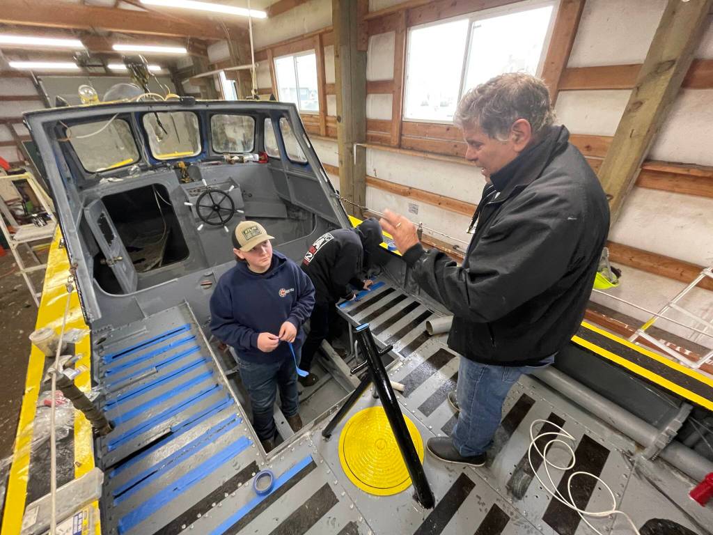 Paul Mirante, instructor for Ocosta High Schools maritime program, directs Logan Johnson as he paints an old Coast Guard lifeboat that students are restoring for display. (Michael S. Lockett / The Daily World)