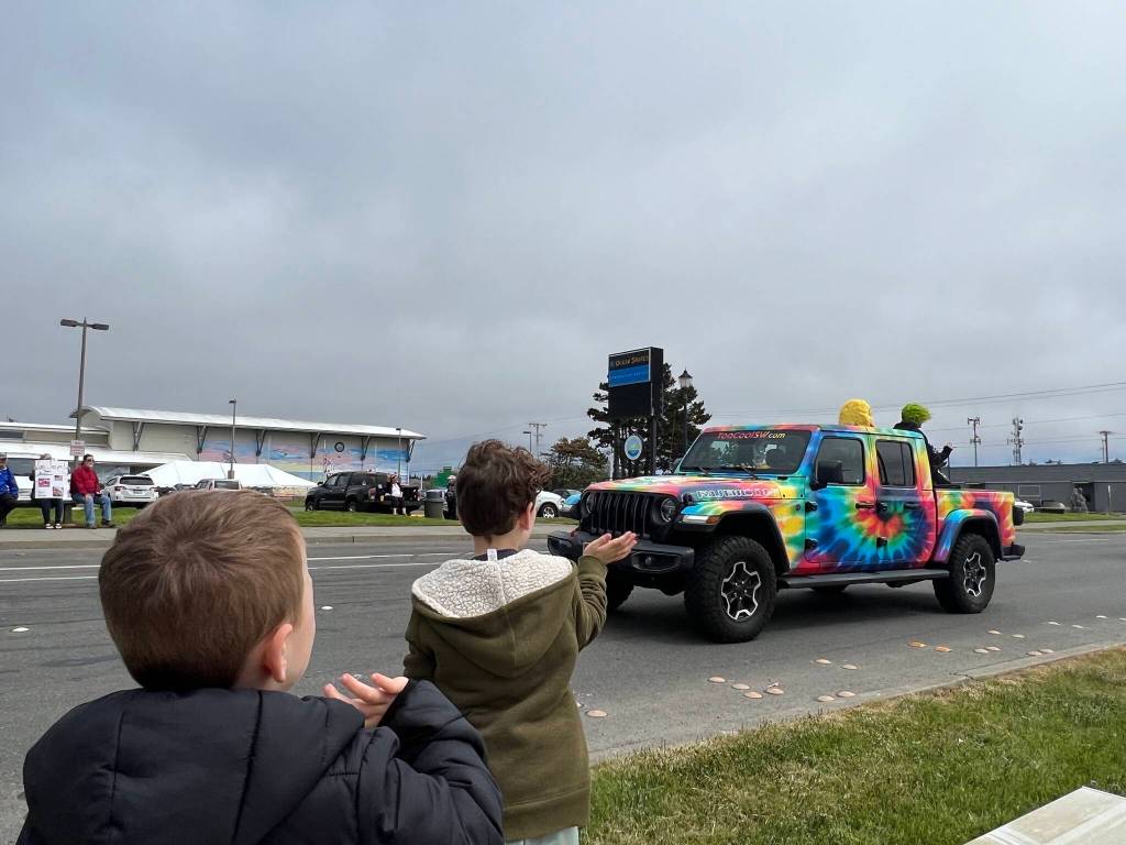 Clayton Franke / The Daily World
From left: Liam and Noah Rook wave to the Too Cool Sportswear Jeep as it heads toward the beach carrying Pam Grgetich and Leo Koch.