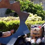 Matthew N. Wells / The Daily World
While one man sleeps on the bronze sculpture titled Illumination by Gerard Tsutakawa  which sits on the corner of East Wishkah and South I streets in downtown Aberdeen  another person looks at the belongings inside a Safeway shopping cart. The city of Aberdeen is in discussions about what to do with the wayward shopping carts seen across Aberdeen.