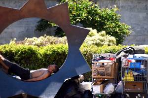 Matthew N. Wells / The Daily World
While one man sleeps on the bronze sculpture titled Illumination by Gerard Tsutakawa  which sits on the corner of East Wishkah and South I streets in downtown Aberdeen  another person looks at the belongings inside a Safeway shopping cart. The city of Aberdeen is in discussions about what to do with the wayward shopping carts seen across Aberdeen.