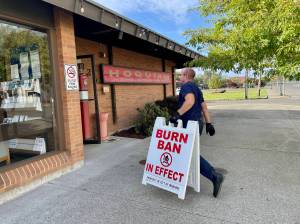 Hoquiam fire Capt. Brandon Ray carries in a burn ban sign as the county eases restrictions with the advent of cooler, damper fall weather on September 19. (Michael S. Lockett / The Daily World)