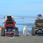 A pair of guests make their way down Westport beach using tracked mobility chairs from Davids Chair, a nonprofit partnering with the city to help bring the beach to more people. (Courtesy photo / John Shaw)