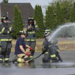 Michael S. Lockett / The Daily World
Derek Jensen of the Hoquiam Fire Department, in blue T-shirt, teaches a group of high schoolers taking part in a fire science program about using a firehose in 2023.