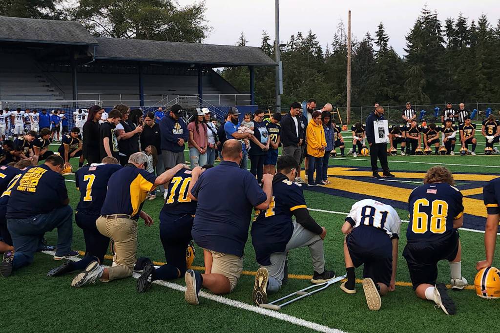 RYAN SPARKS / THE DAILY WORLD The Aberdeen Bobcats take a knee while surrounding members of Bob Delahanty family after the longtime Aberdeen chain crew organizer was remembered with a moment of silence before a game against Olympic on Friday in Aberdeen.