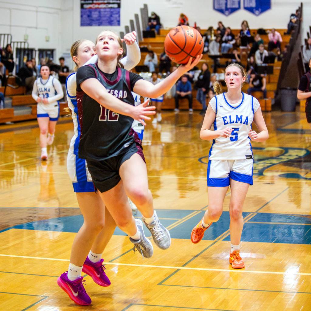 PHOTO BY MIKE ROBERTS Montesano sophomore point guard Tieander Olson (12) glides to the hoop against Elmas Amaya Lewis and Mikayla Roberts (5) during the Bulldogs 40-21 victory on Thursday in Elma.