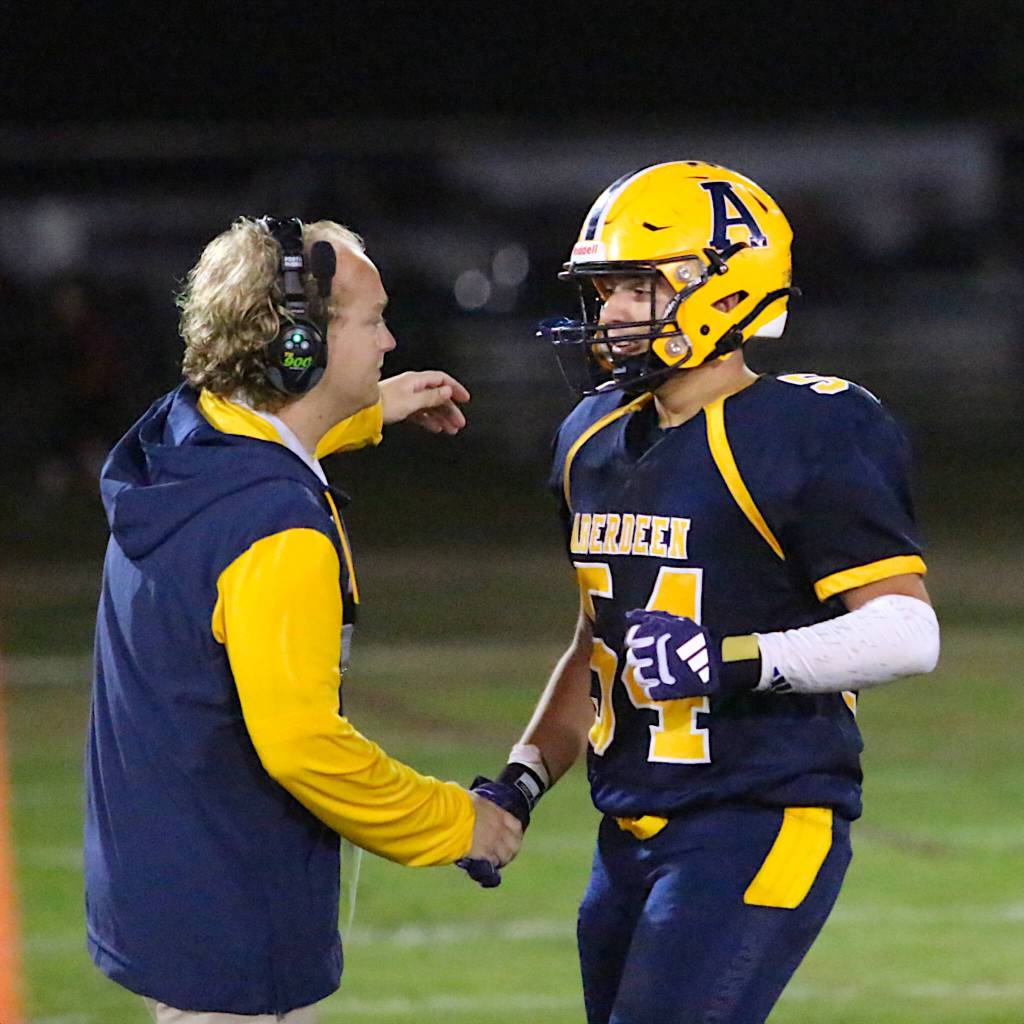 RYAN SPARKS | THE DAILY WORLD Aberdeen senior Jack Dawson (54) is greeted by offensive coordinator Macoy Gonseth after Dawson joined the team huddle for a play during the fourth quarter of a 43-7 win over Hoquiam. It was the last time Dawson will play football for the Bobcats as he is scheduled to undergo knee surgery this week.